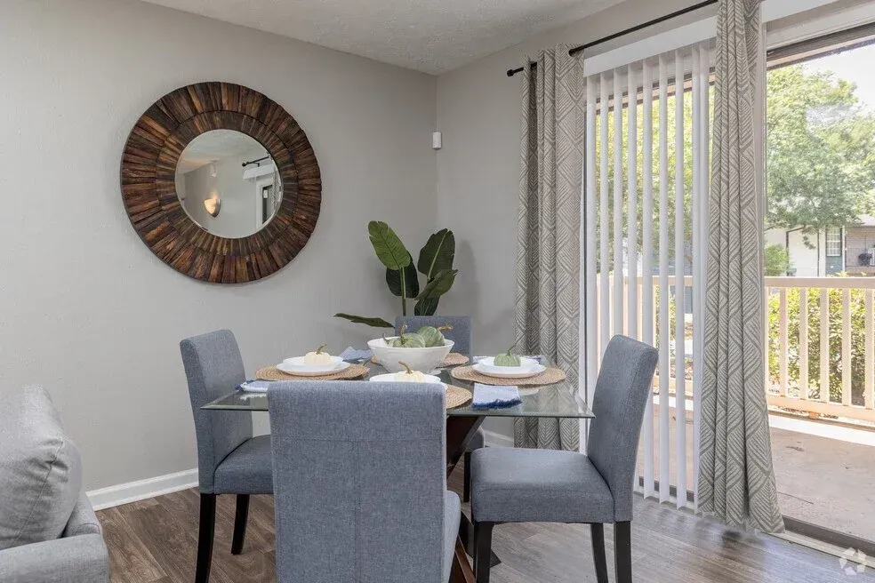 Dining area with round glass table, four gray chairs, wall mirror, and sliding door to a patio.