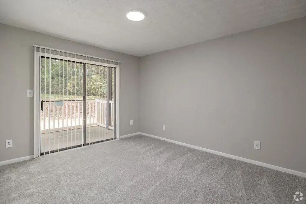 Empty gray carpeted room with sliding glass door to a balcony and recessed ceiling light