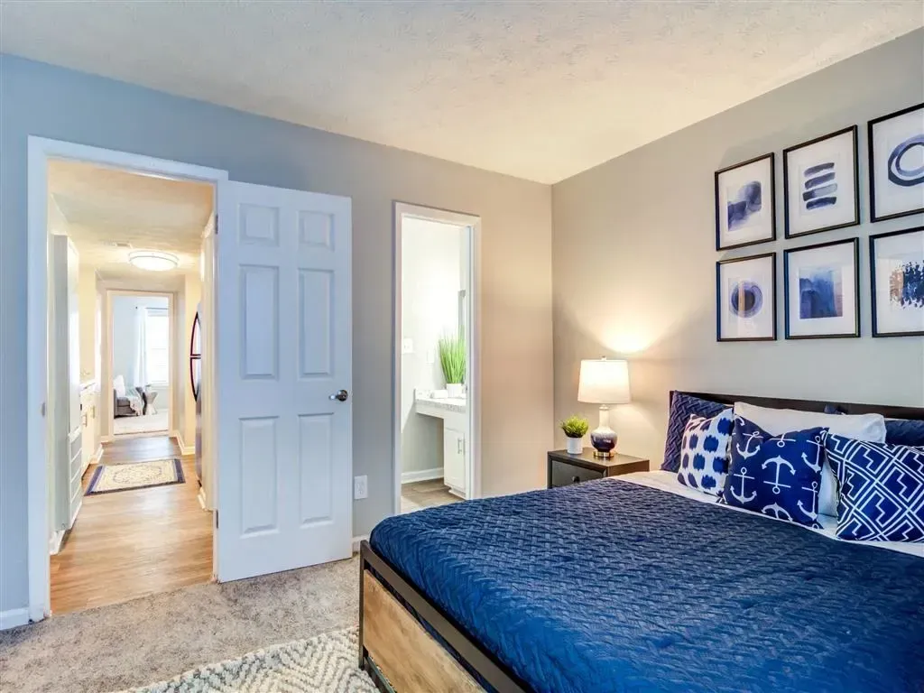 Bright bedroom with blue bedding, framed wall art, and an open door to a hallway and bathroom