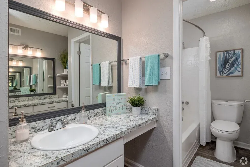 Bright bathroom with granite vanity, large mirror, towel rack, and a toilet in a separate alcove.