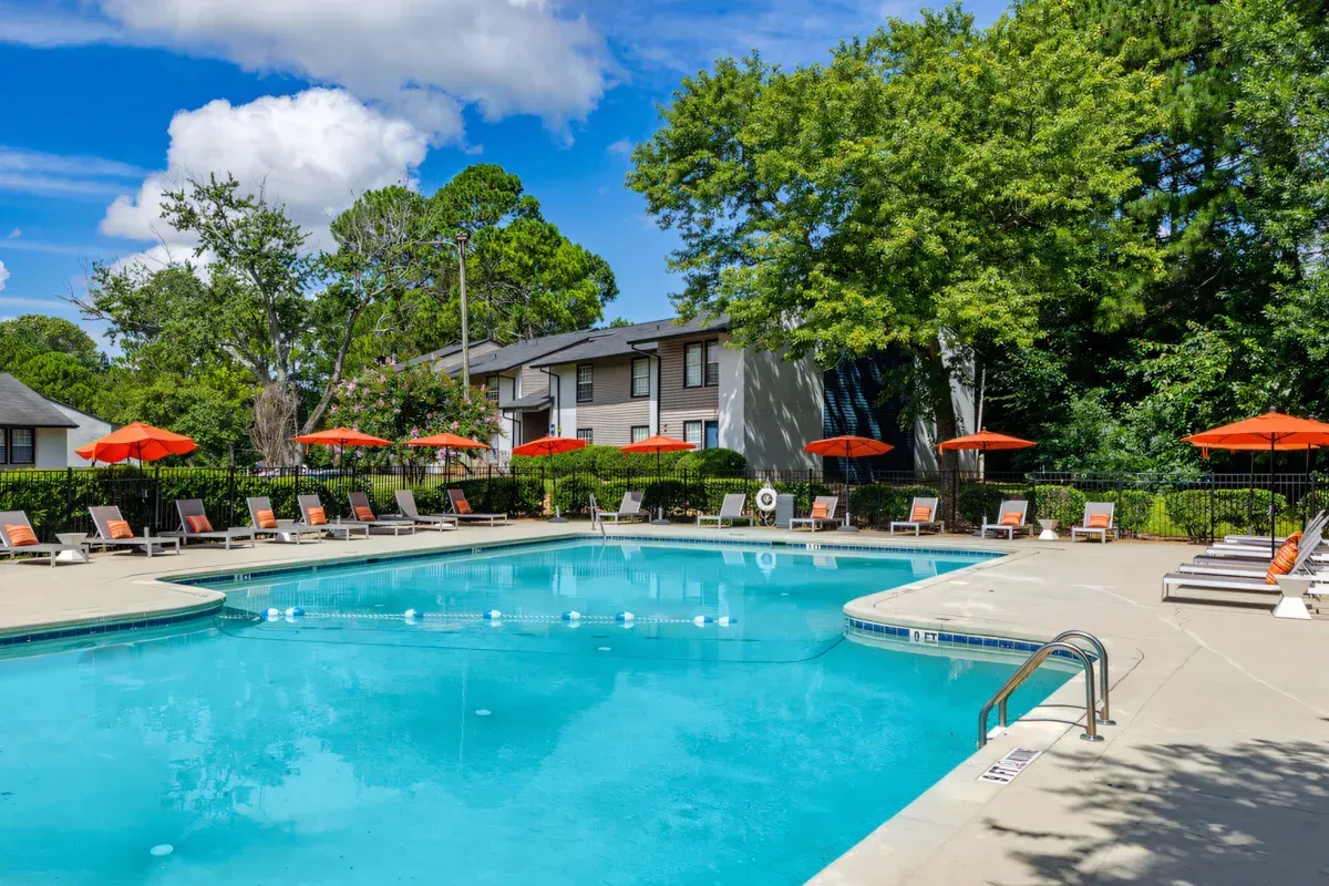 Outdoor hotel pool with lounge chairs, orange umbrellas, and apartment buildings under a blue sky