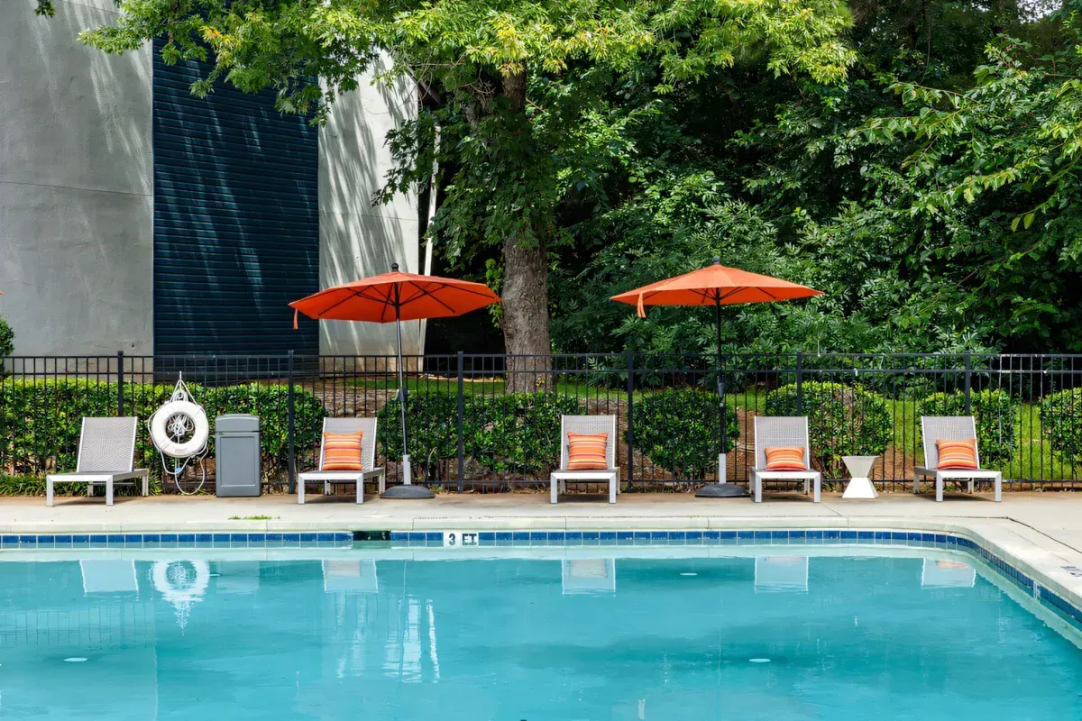 Poolside lounge chairs under orange umbrellas beside a turquoise swimming pool