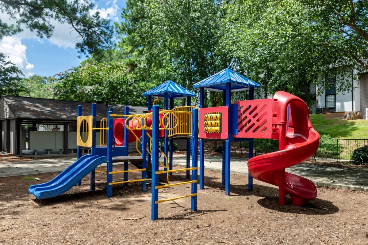 Colorful playground with blue slides, red spiral slide, and climbing structures under trees in a park
