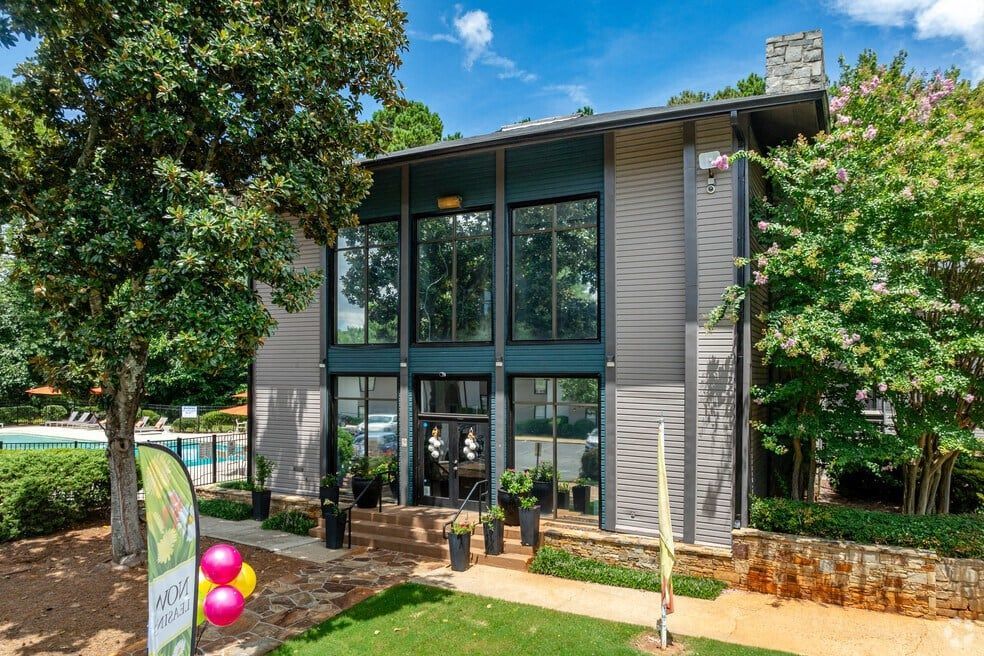 Modern two-story house with large windows, front patio, and trees in the yard