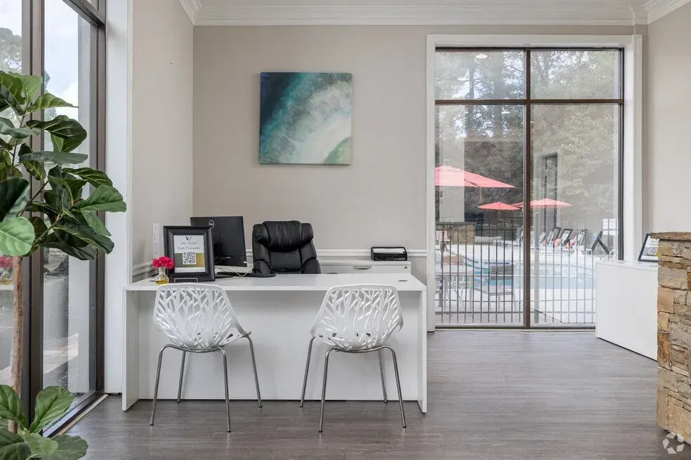 Modern home office with white desk, two chairs, wall art, and large sliding glass doors to a patio.