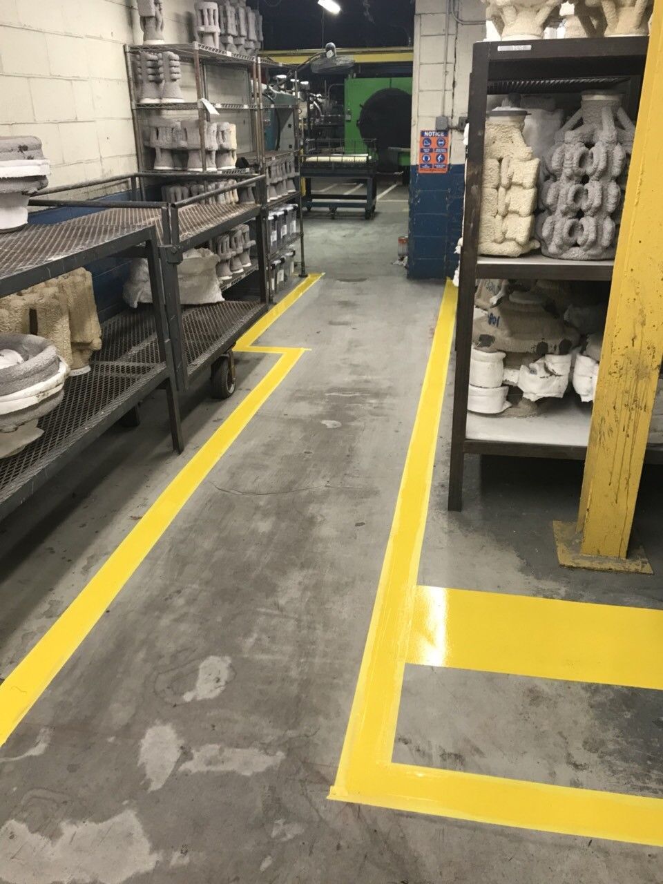 Warehouse aisle with yellow safety lines, metal shelving, and stacked white parts or supplies