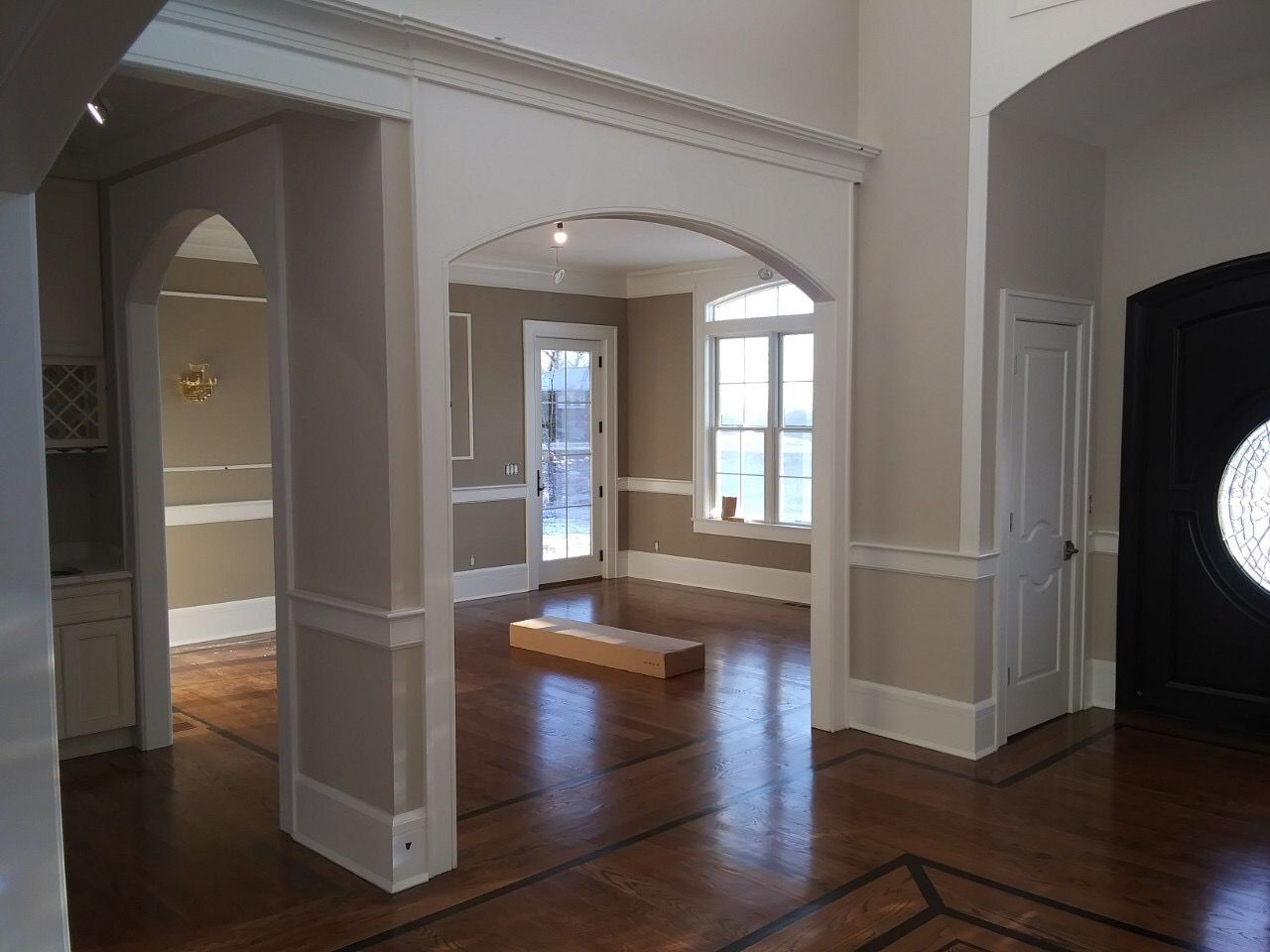 Empty living room with hardwood floors, arched openings, and large windows letting in daylight