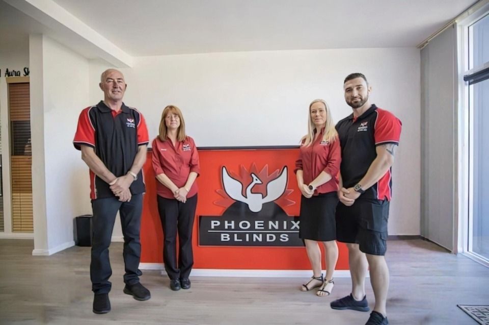 A Group of People Standing in Front of a Phoenix Blinds Sign — Phoenix Blinds In Albion Park Rail, NSW