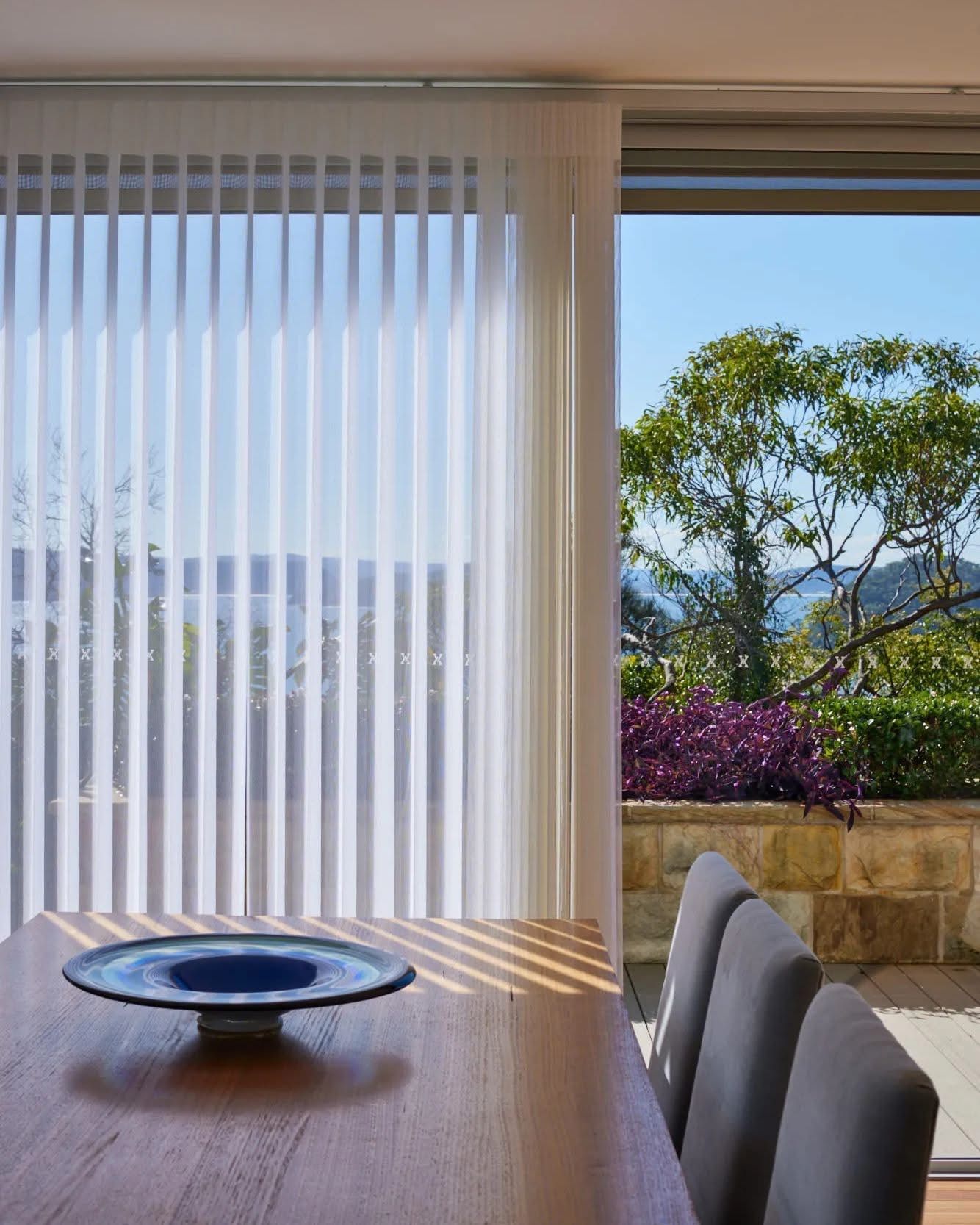 A dining room table with a bowl on it in front of a window with vertical blinds — Phoenix Blinds In Albion Park Rail, NSW