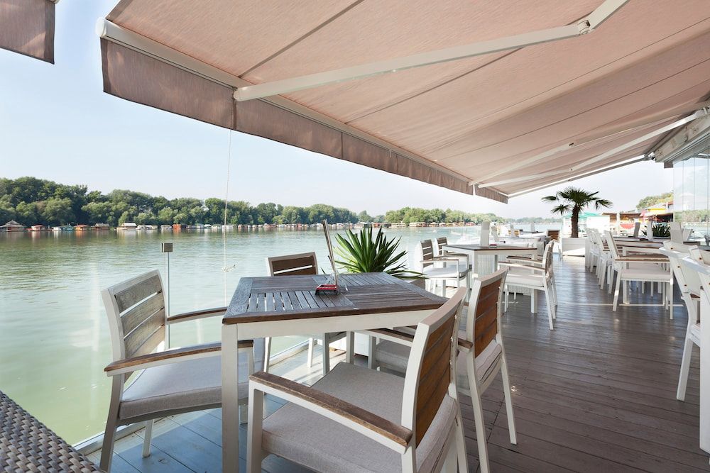 A Restaurant with Tables and Chairs Under an Awning Overlooking a Body of Water — Phoenix Blinds In Albion Park Rail, NSW