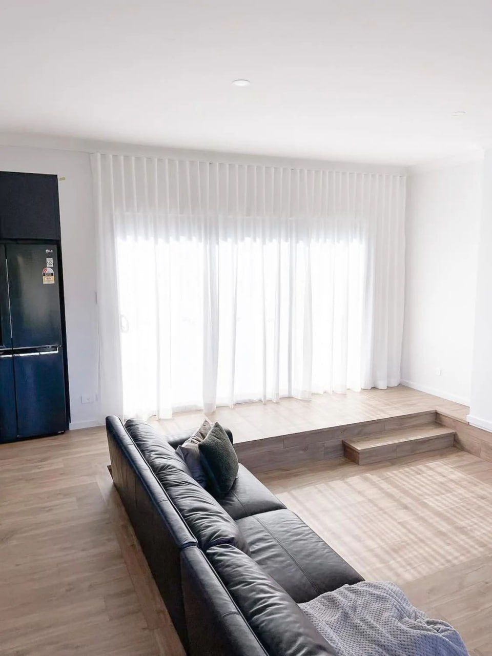 A Living Room with A Black Couch and White Curtains — Phoenix Blinds In Albion Park Rail, NSW