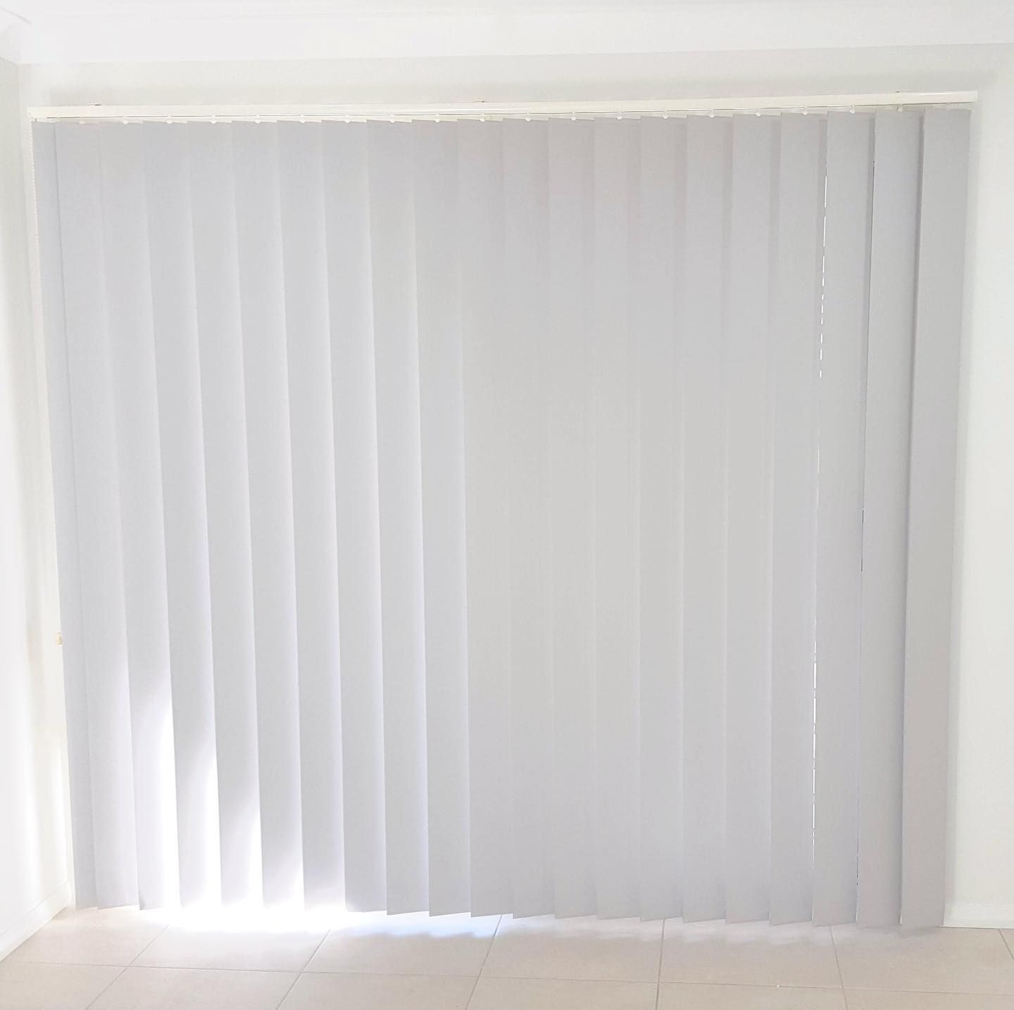 A White Vertical Blind Is Hanging on A Window in A Room — Phoenix Blinds In Albion Park Rail, NSW