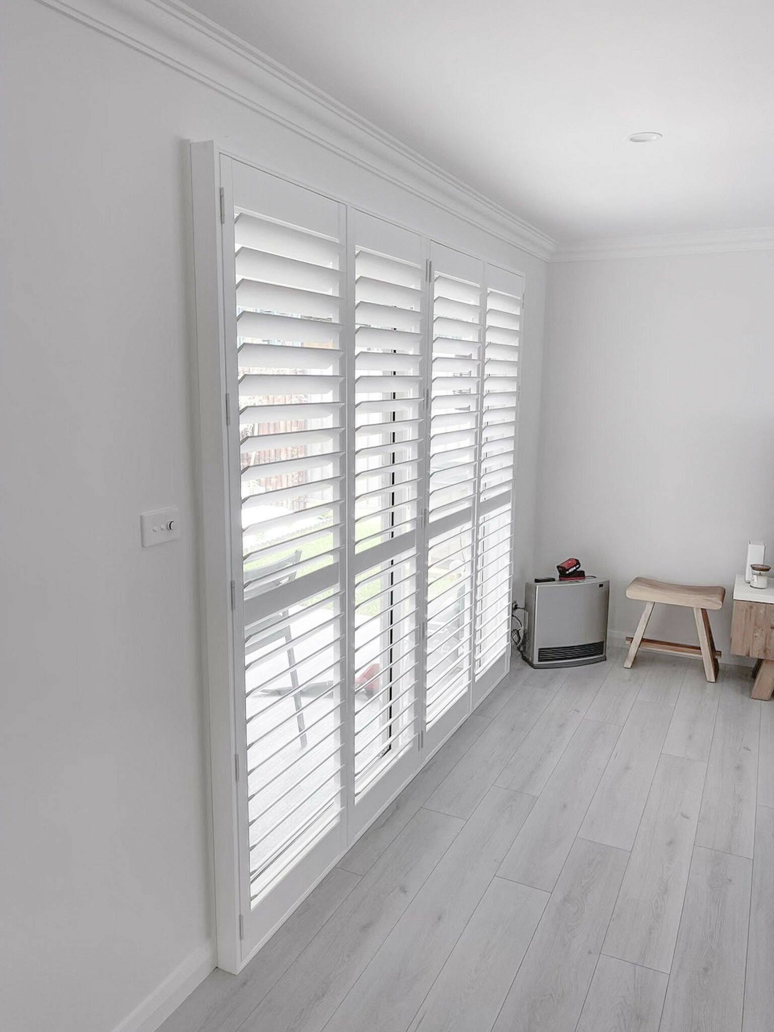 A Room with White Shutters on The Windows and A Wooden Bench — Phoenix Blinds In Shellharbour, NSW