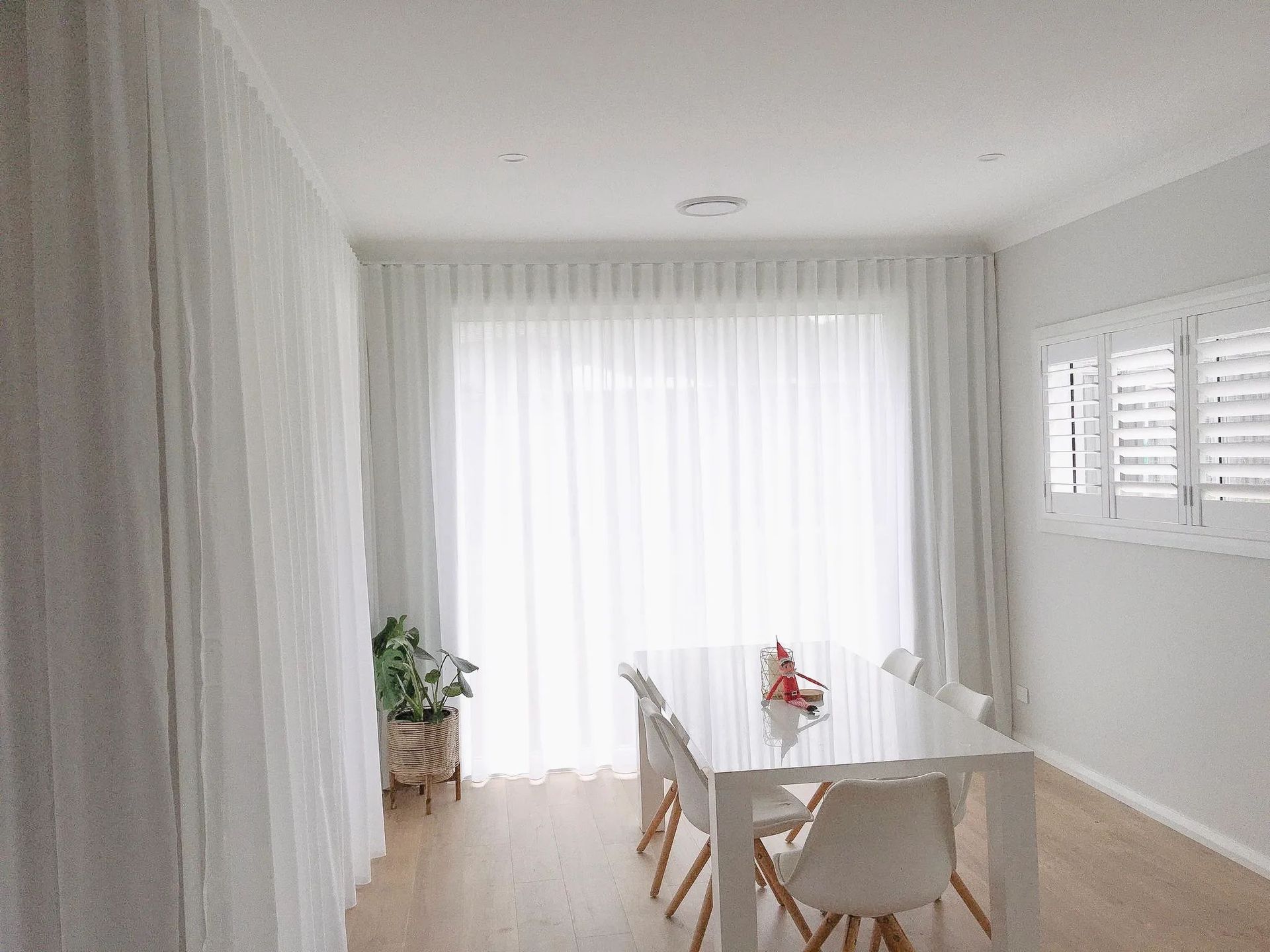 A Dining Room with A Table and Chairs and White Curtains — Phoenix Blinds In Woonona, NSW
