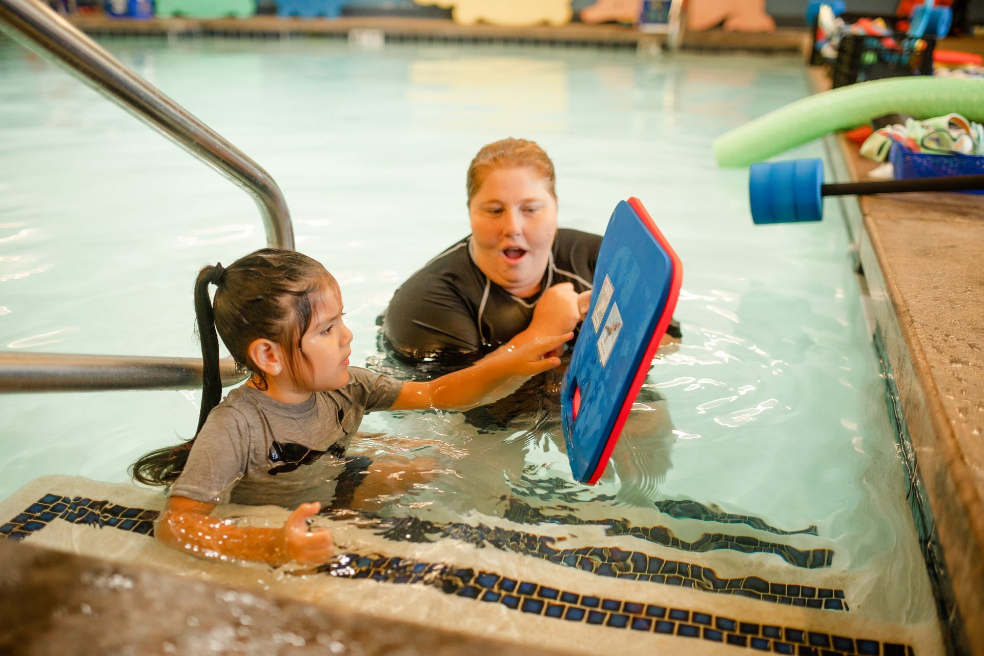 A woman is teaching a little girl how to swim in a swimming pool.