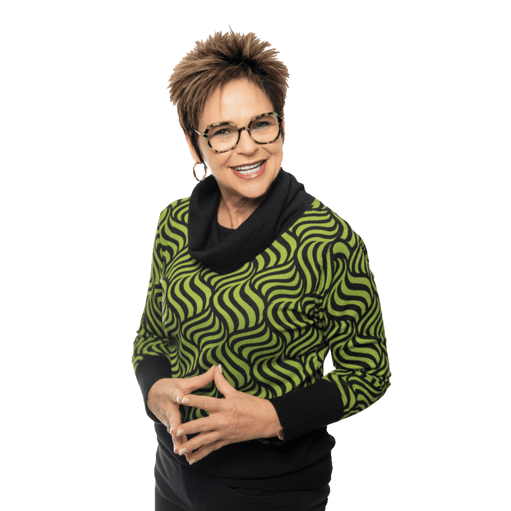 A person wearing glasses and a green and black patterned sweater, smiling with hands clasped, against a white background.