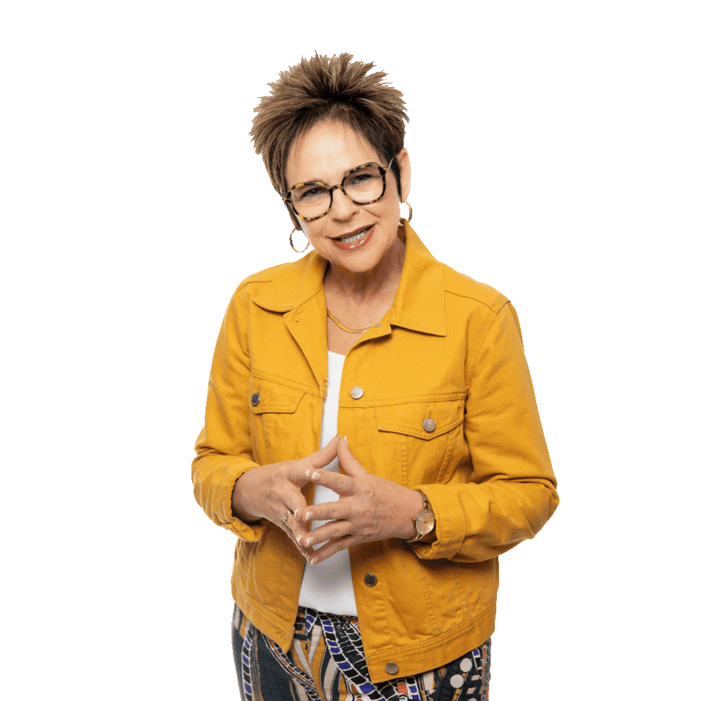 A person wearing glasses and a mustard-yellow jacket stands against a white background with their hands clasped together.