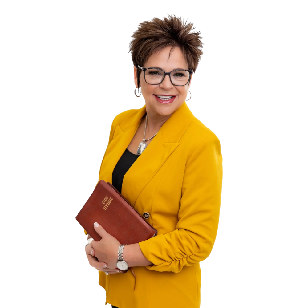 A smiling person with short, dark hair wearing glasses and a yellow blazer, holding a Bible against a white background.