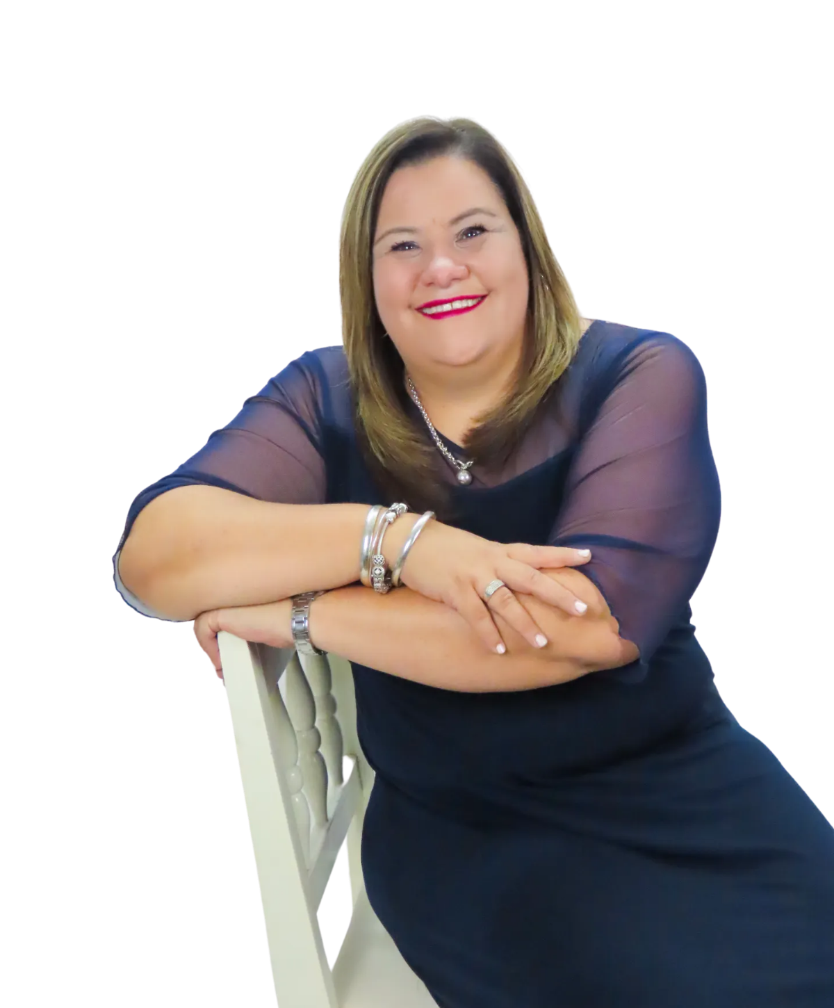 A smiling person with shoulder-length hair wearing a dark blue dress with sheer sleeves, leaning on a white chair.