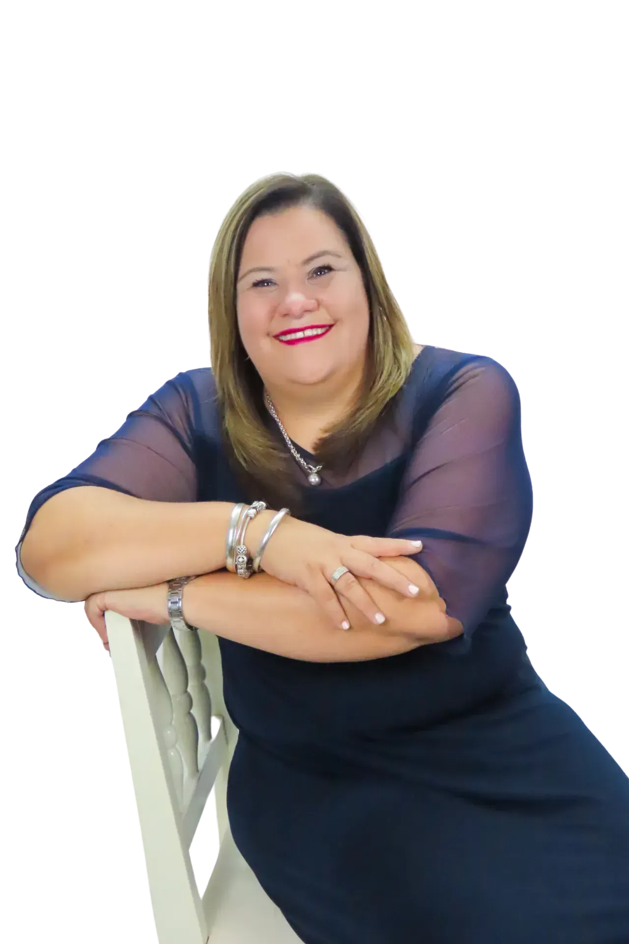 A woman in a navy dress with sheer sleeves smiles while resting her arms on the back of a light-colored chair.