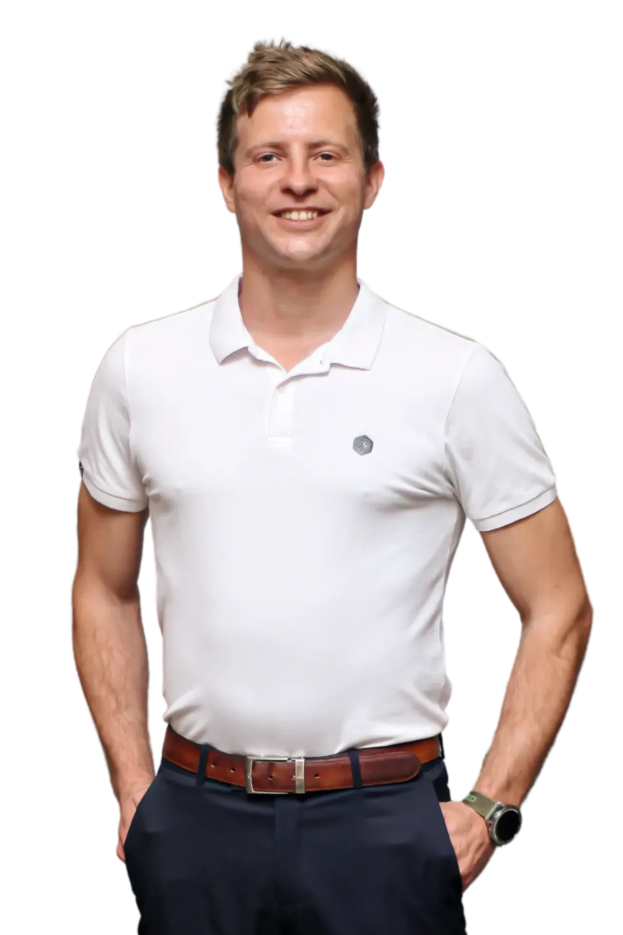 A person smiling, wearing a white polo shirt and blue trousers with a brown belt, hands tucked in pockets, isolated.