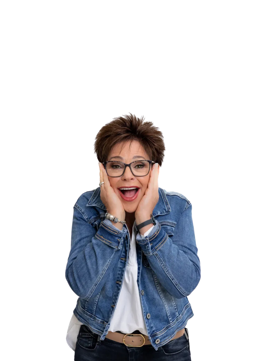 Person in a blue denim jacket and glasses, smiling with hands on cheeks against a white background
