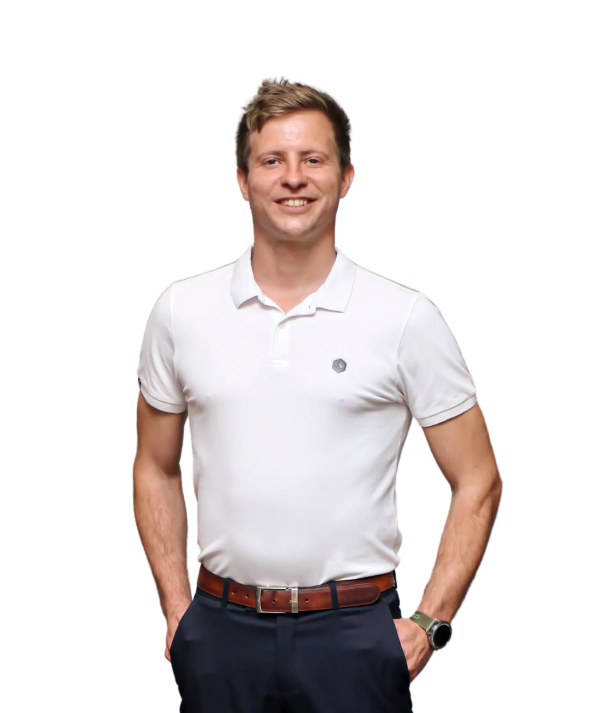 A person smiling, wearing a white polo shirt and blue trousers with a brown belt, hands tucked in pockets, isolated.