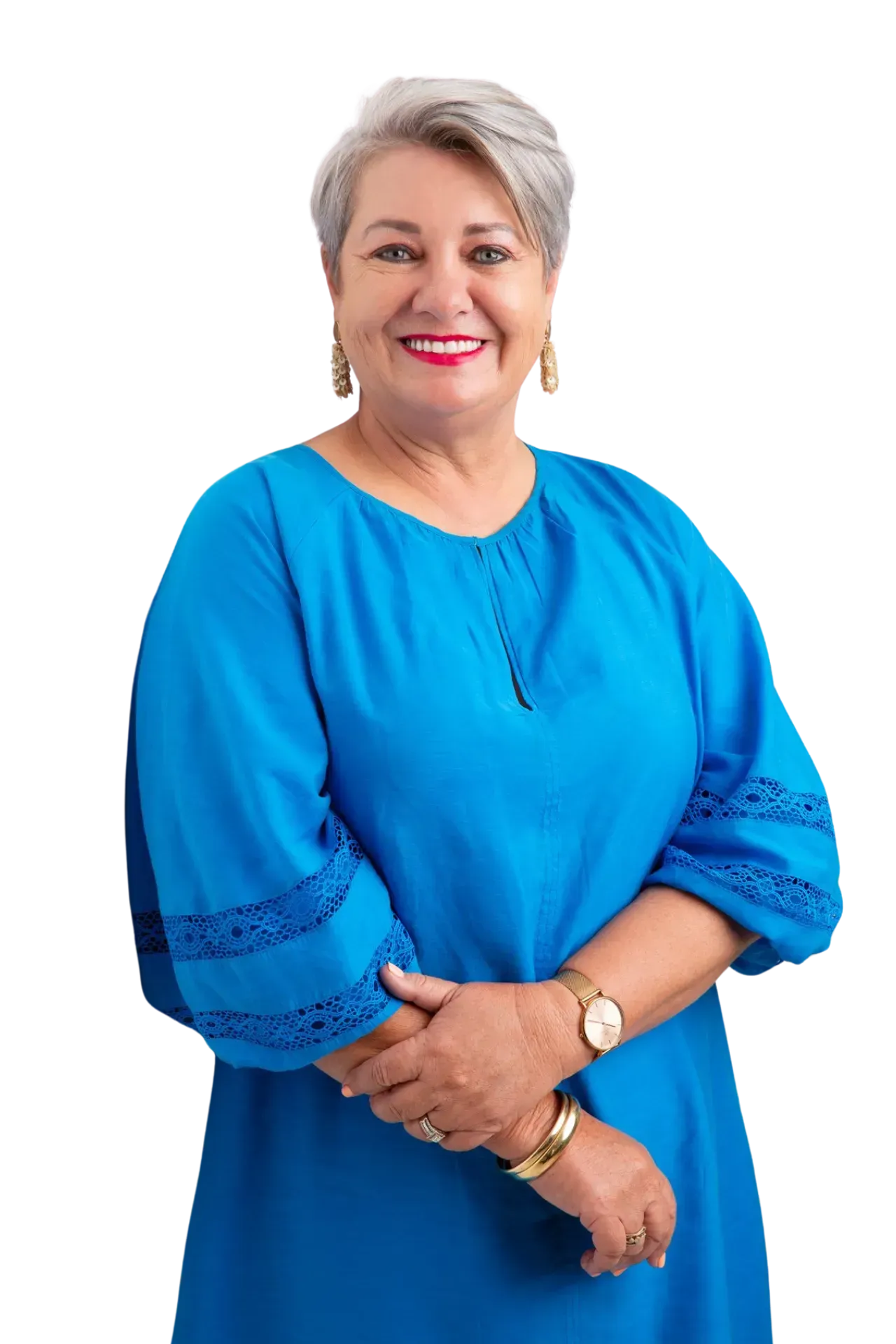 A smiling person with short gray hair, wearing a bright blue long-sleeved dress and gold jewelry