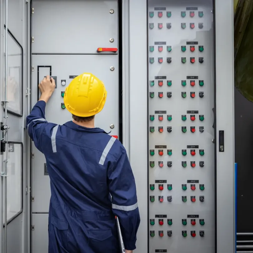 Un operaio con tuta blu e casco giallo aziona un quadro elettrico di controllo.