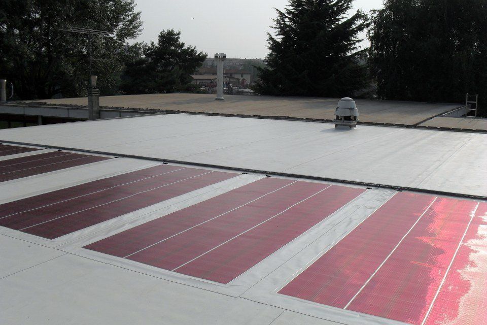 Tetto con grandi pannelli solari rossi e una piccola unità di ventilazione, circondato da alberi.