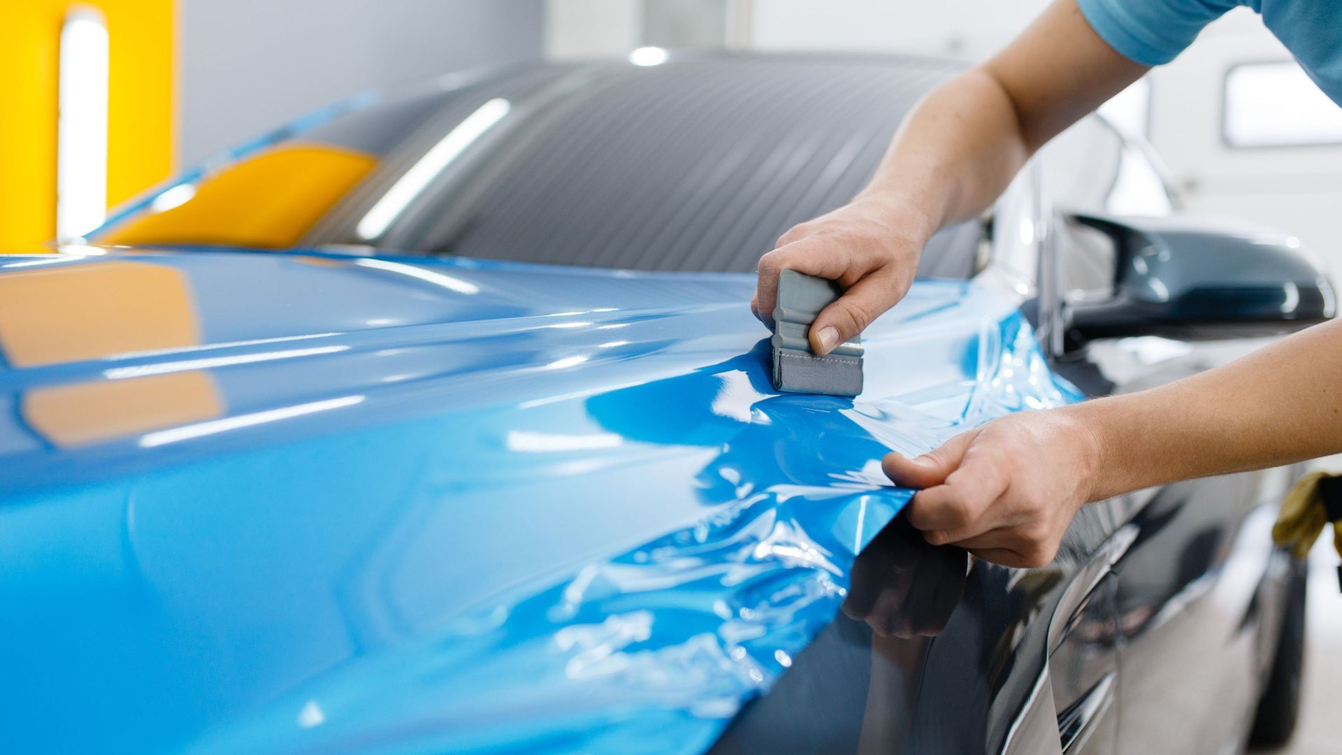 A person wrapping a blue film on a car in a shop.
