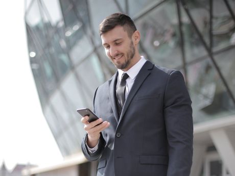 A man in a suit and tie is looking at his cell phone.