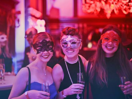 Three women wearing masks and holding champagne glasses are posing for a picture.