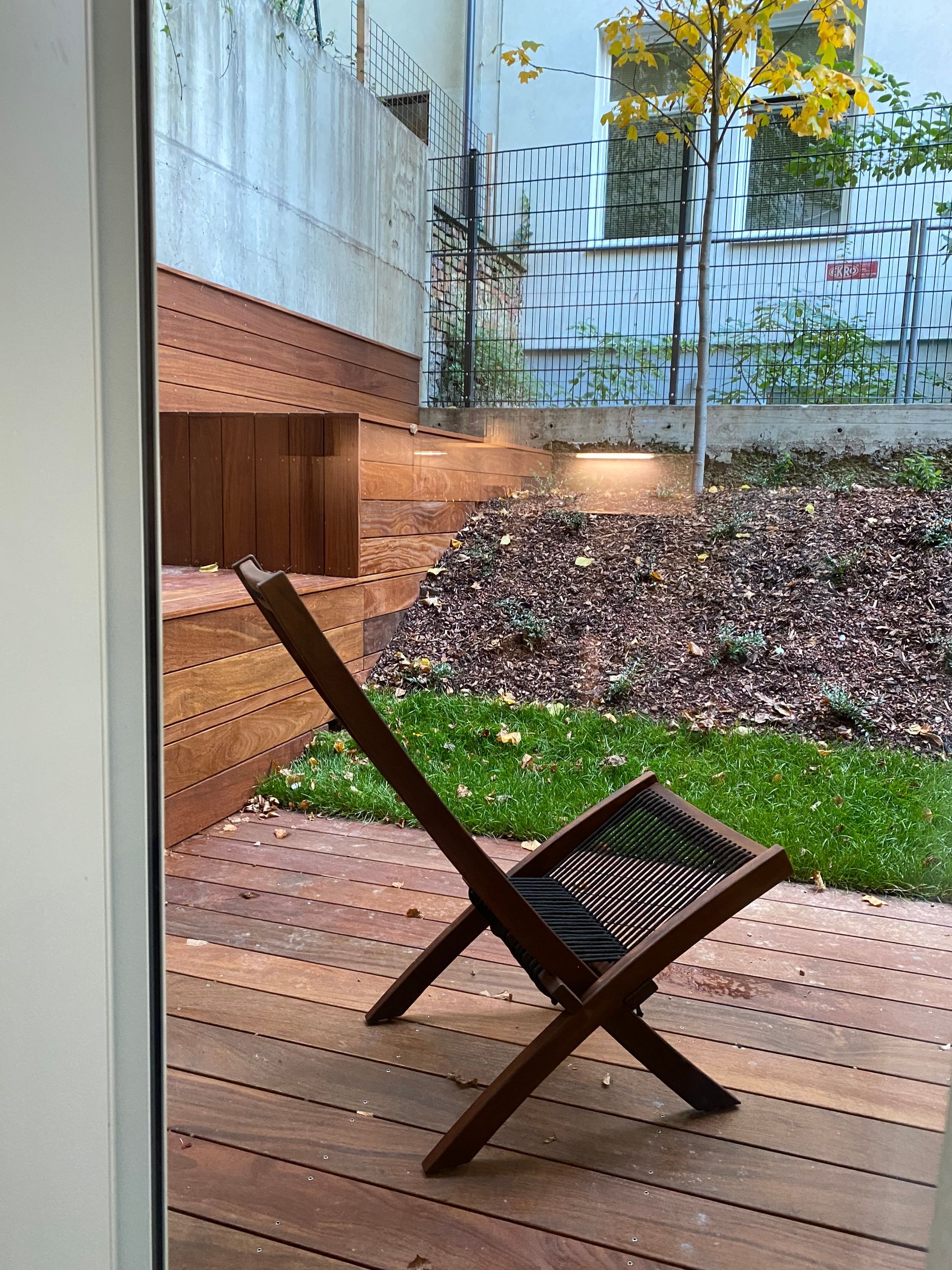 A wooden chair is sitting on a wooden deck next to a window.