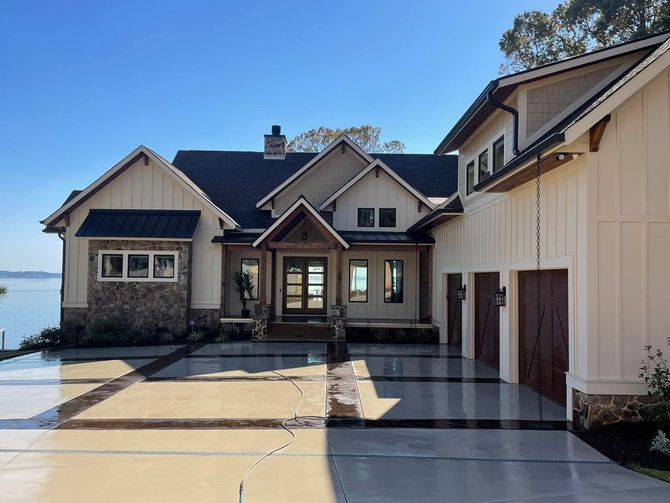 Beige and stone home with dark roof, and garage doors, on a sunny day.