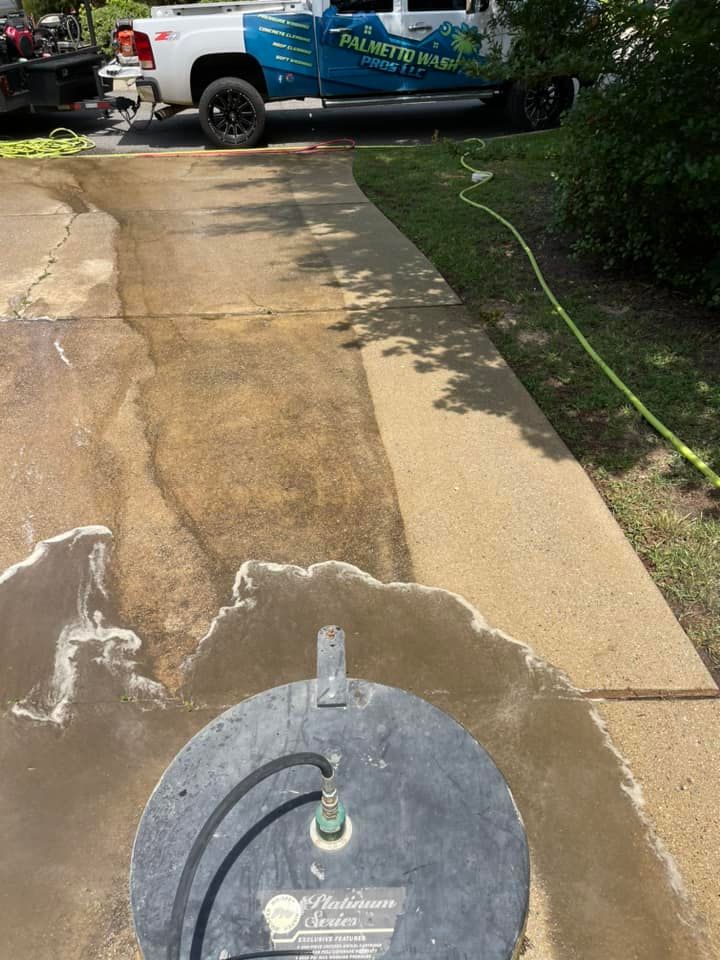 A pressure washer cleaning a concrete driveway. A truck with a company logo is parked nearby.
