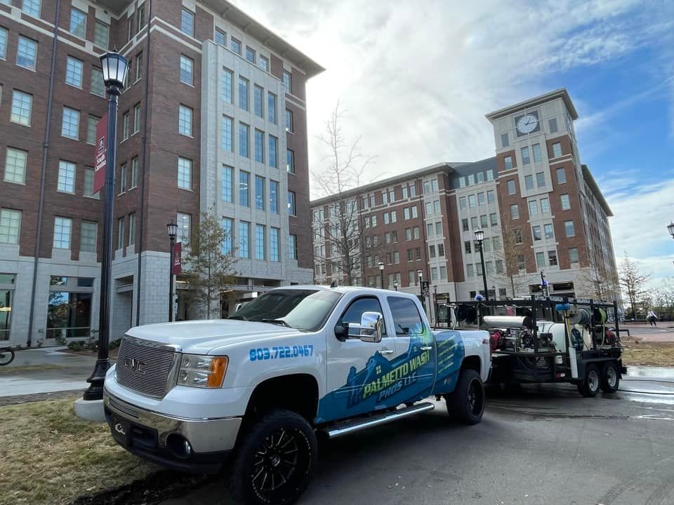 White pickup truck with blue and green graphics parked outside brick buildings.