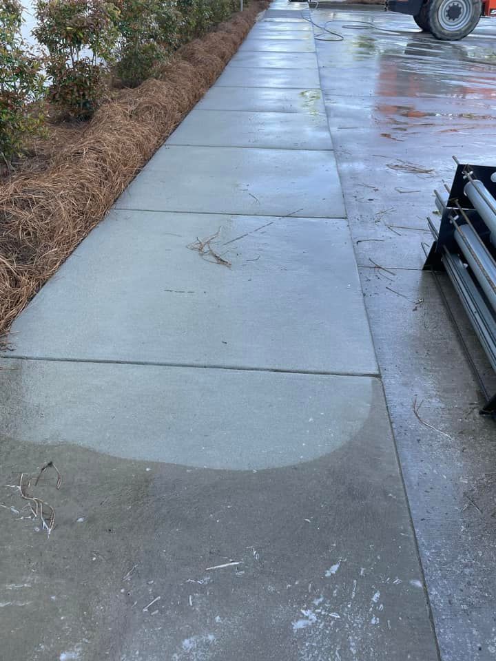 Wet concrete sidewalk with mulch and bushes on one side, metal beams on the right.