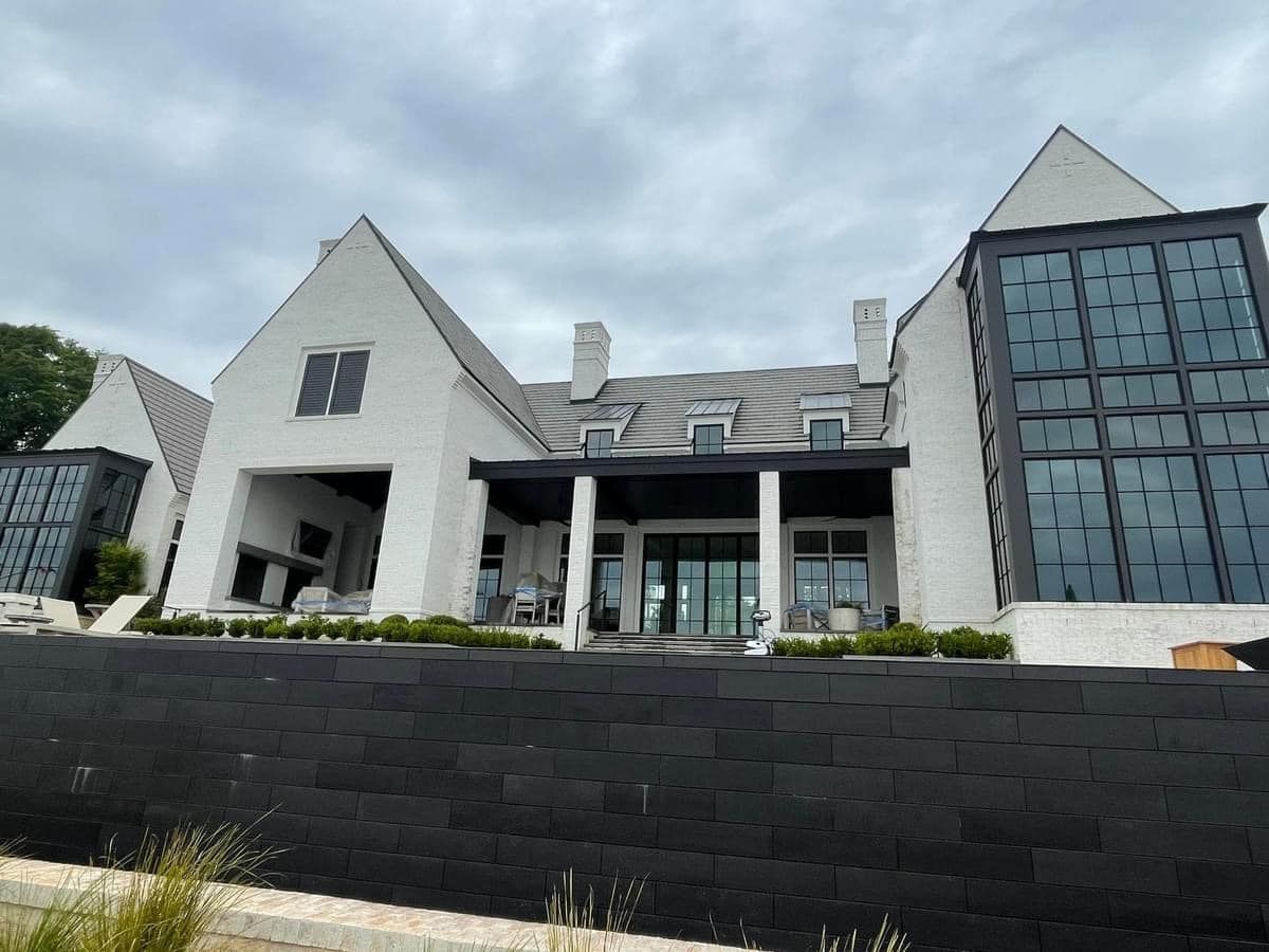 White brick house with black windows, a porch, and black retaining wall. Overcast sky.