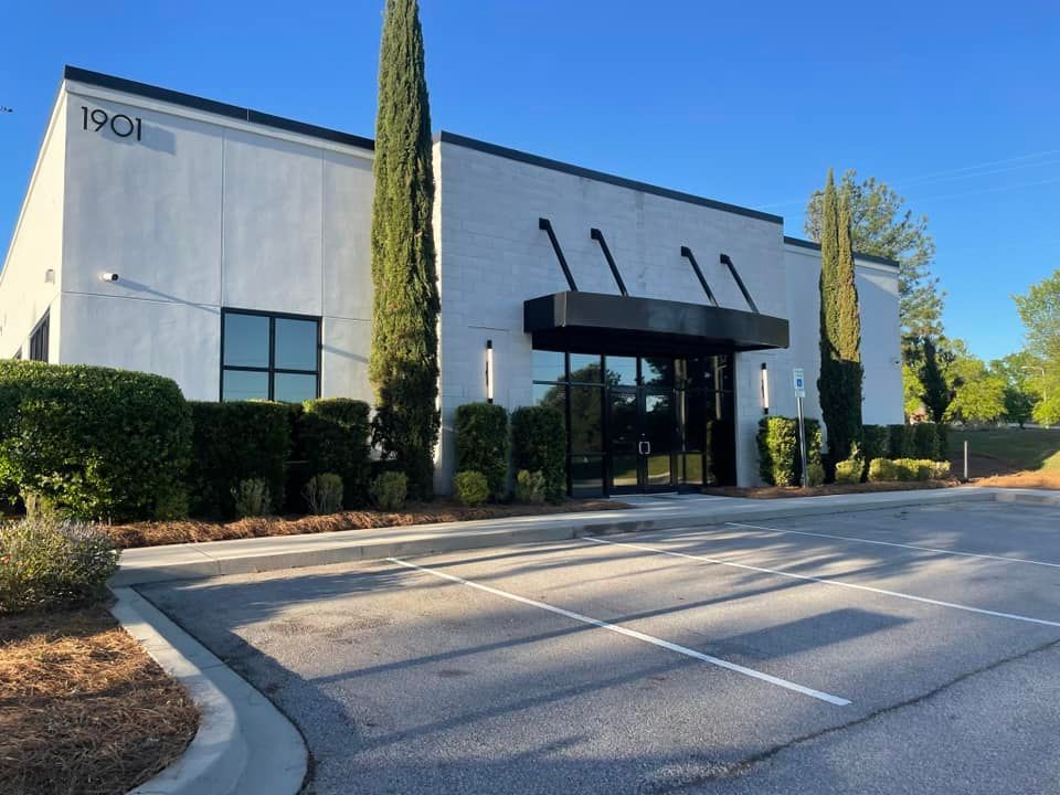 Exterior view of a modern white building with black accents, glass doors, and manicured landscaping.