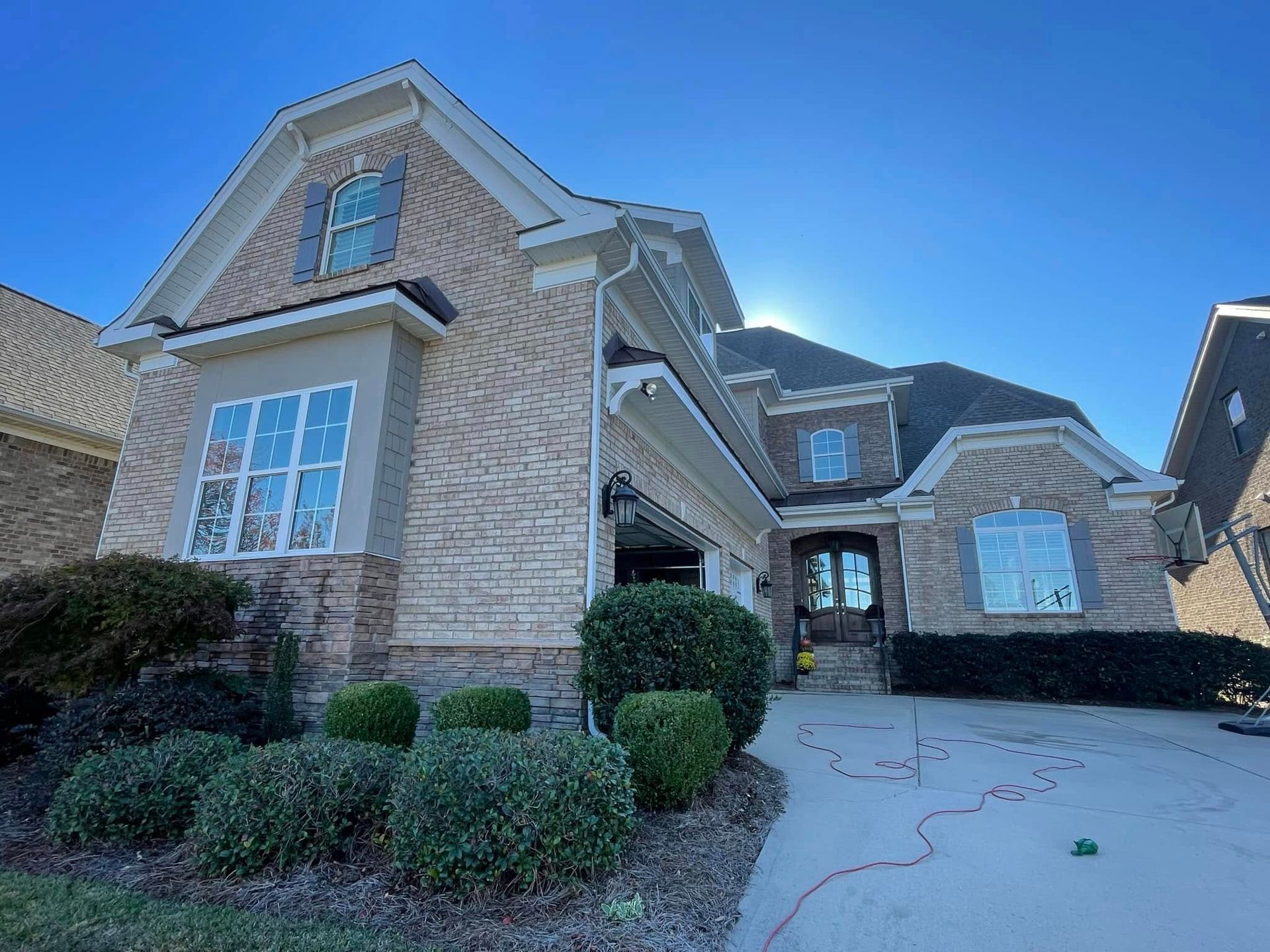 Two-story brick house with blue shutters, a driveway, and landscaping under a clear sky.