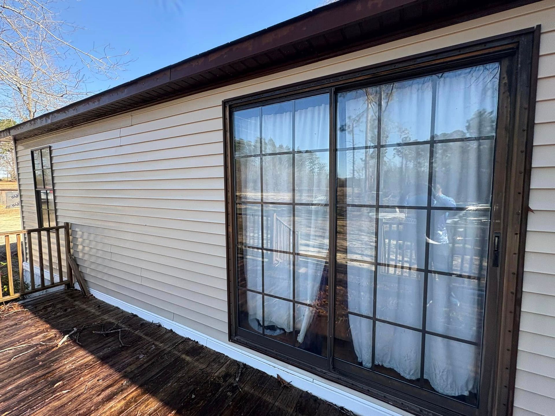Beige siding with brown trim surrounds a sliding glass door and deck. White curtains inside.