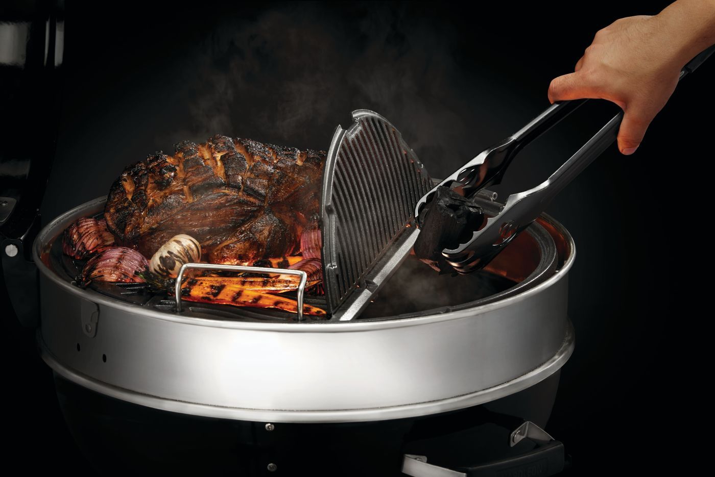 Persona che usa le pinze per girare la carne su una griglia metallica posta sul fuoco. Il vapore sale.