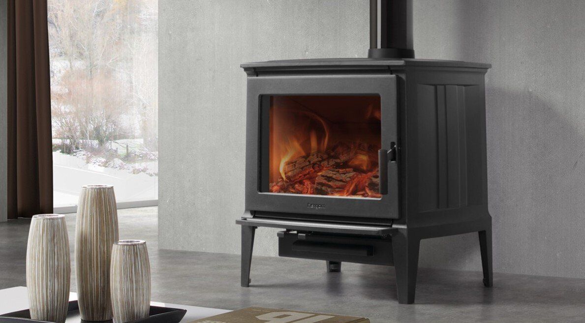 Stufa a legna nera con fuoco all'interno; stanza dai toni neutri con vasi decorativi.