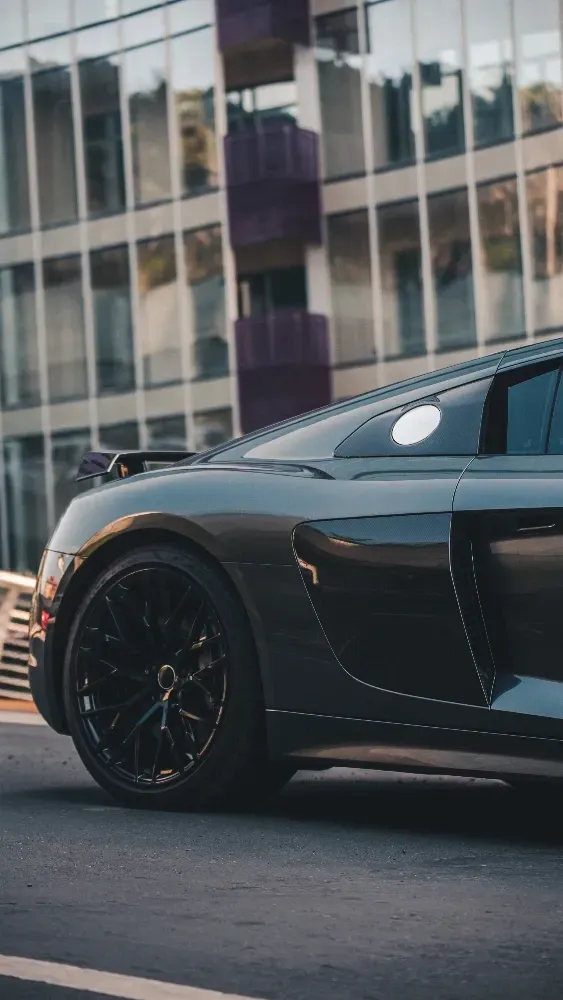 A black sports car is parked in front of a building that has a Paint Protection Film (PPF) applied to it.