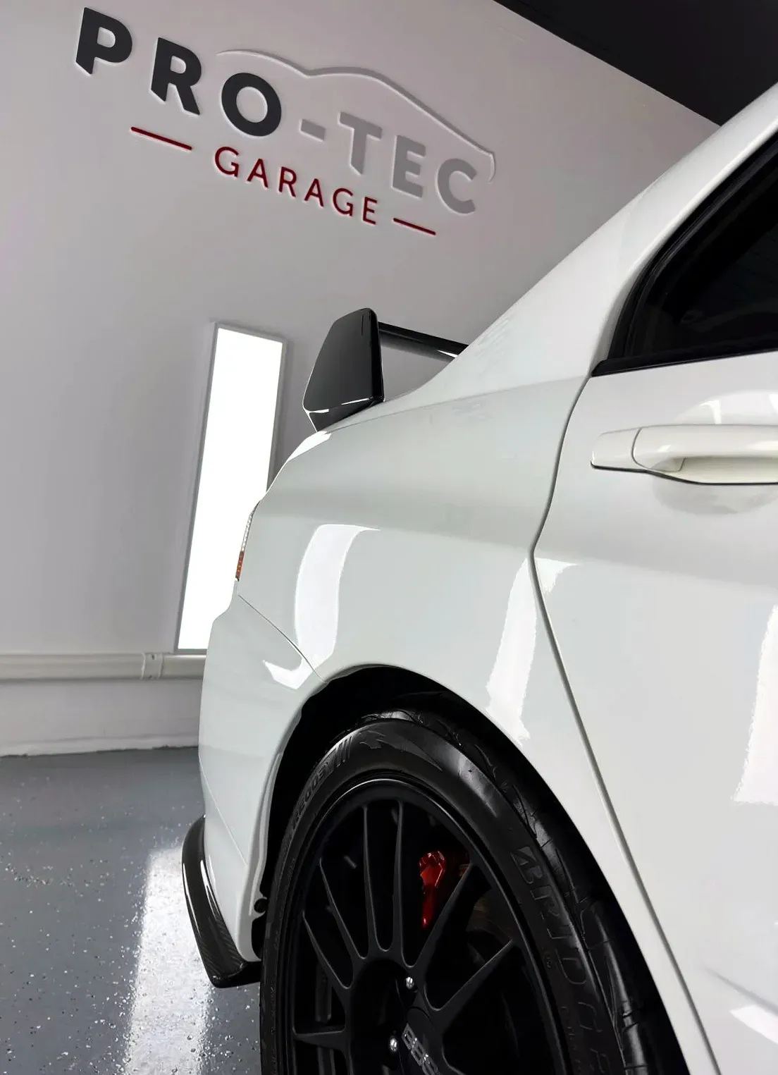 A white car is parked in front of a pro-tec garage sign