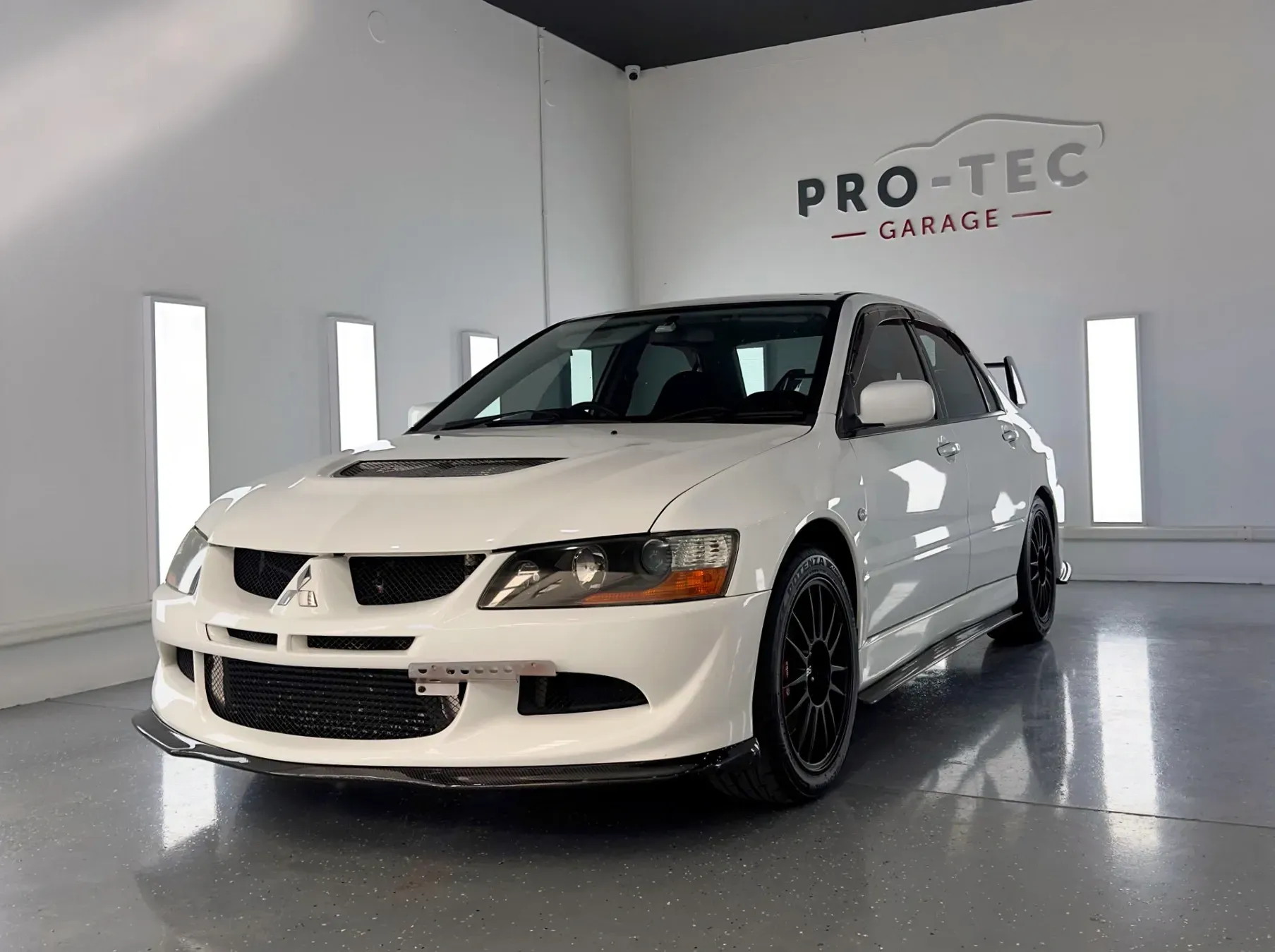 A white car is parked in front of a pro-tec garage after applying PPF & Ceramic Coating Services near the North Rocks.