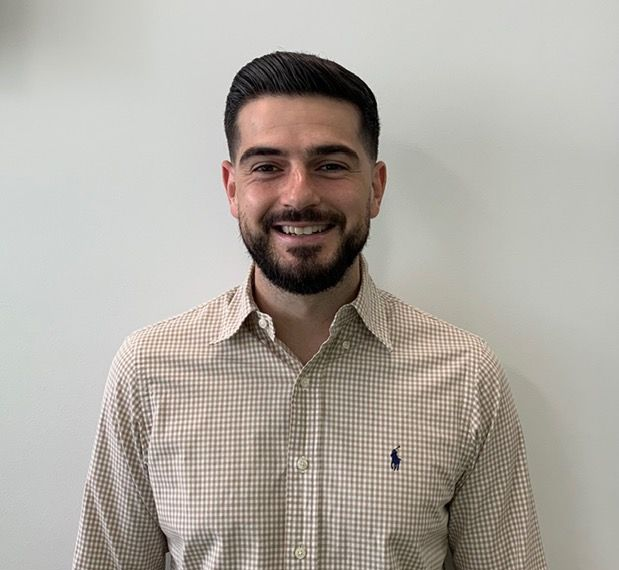 a young man with a beard is smiling for the camera while wearing a blue shirt .