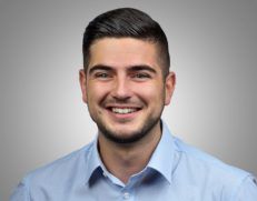 a young man with a beard is smiling for the camera while wearing a blue shirt .