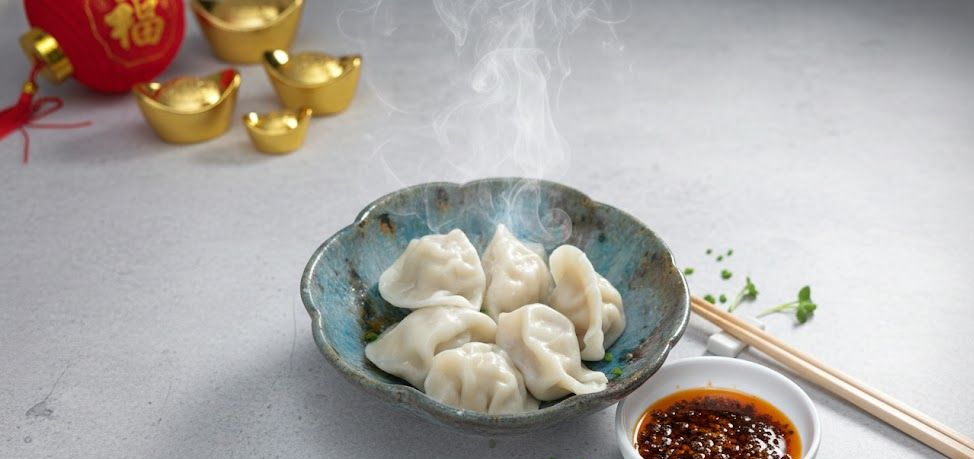 藍色碗中盛著熱氣騰騰的餃子,配有蘸醬、筷子和金元寶,可能是為慶祝中國新年準備的。